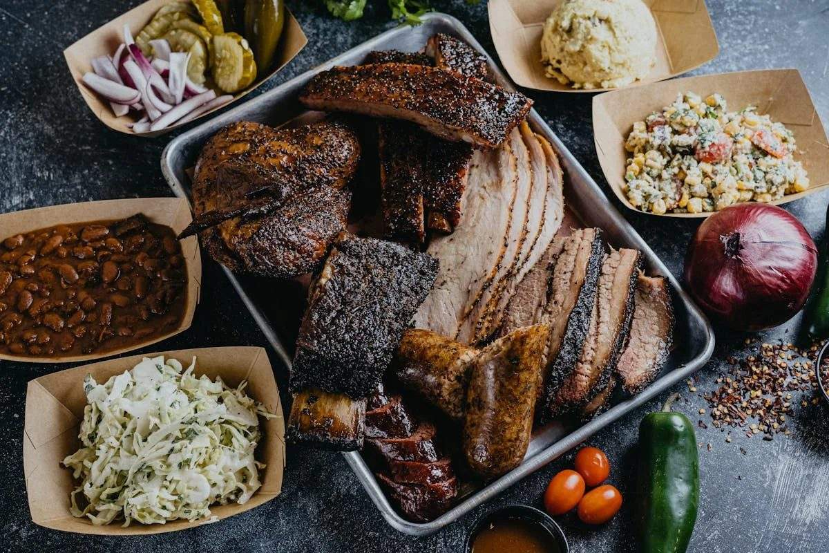 A tray of sliced brisket, ribs, smoked turkey and sausage with sides at 1701 Barbecue in Beaumont
