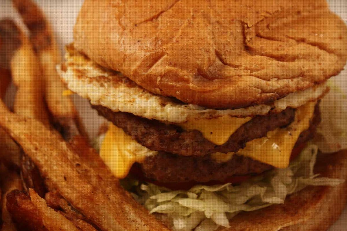 A double cheeseburger topped with a fried egg, next to hand-cut fries