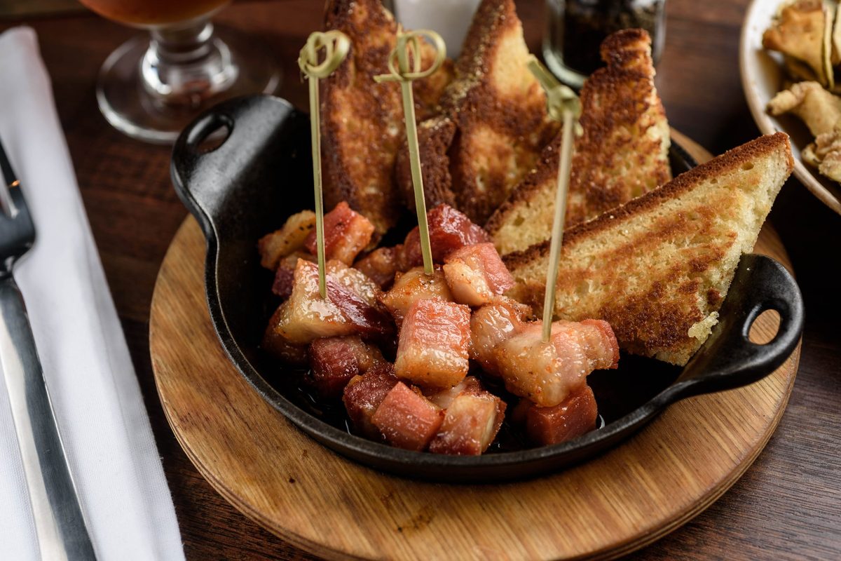 Man Candy, smoked pork belly bites on skewers in a cast-iron skillet with toast points, at J. Wilson's in Beaumont