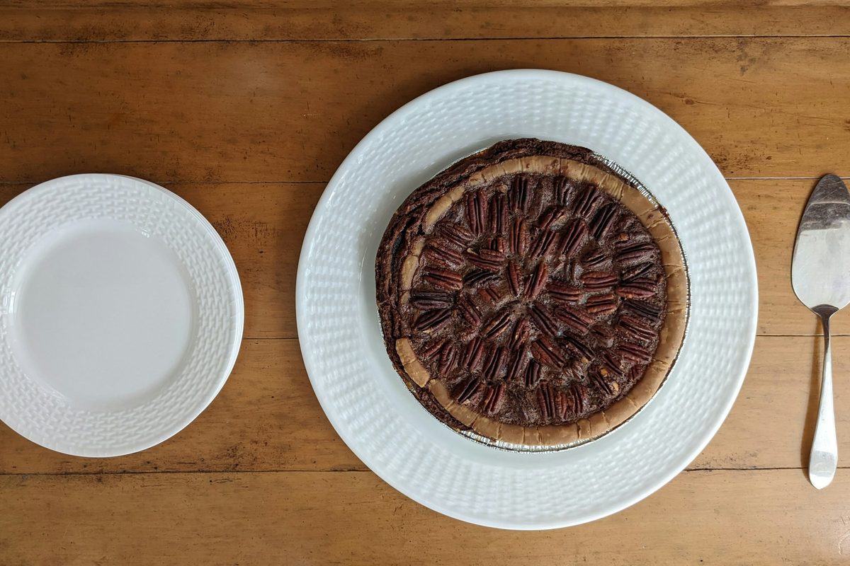 A whole pecan pie on a white plate with a pie server