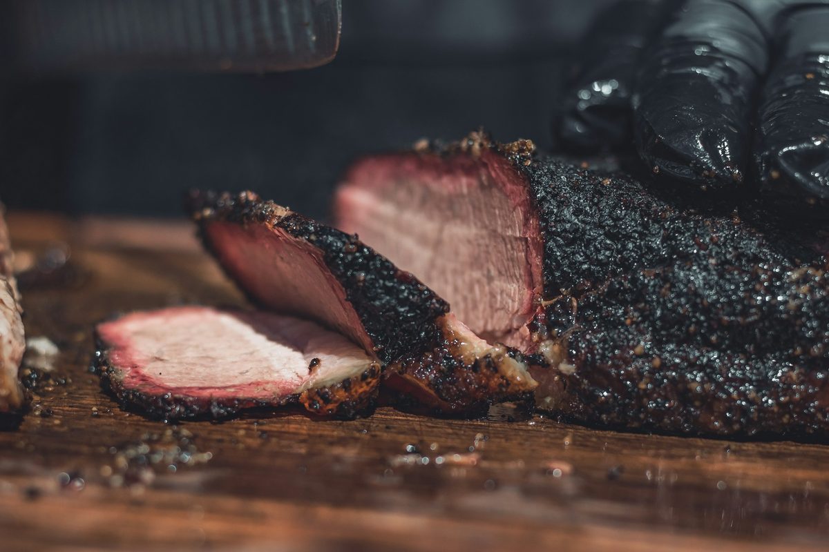 Sliced smoked brisket with a dark bark and a pink smoke ring on a cutting board