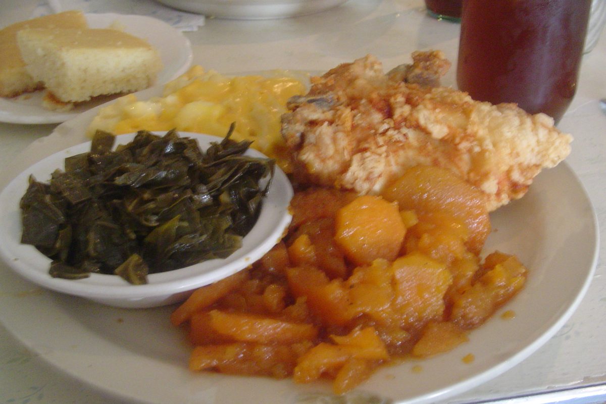 A soul food plate with fried chicken, collard greens, candied yams, macaroni and cheese and cornbread