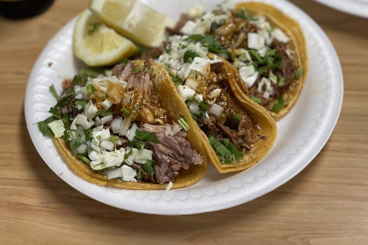 Three corn tortilla tacos with shredded meat, onion, cilantro and green salsa, with lime wedges