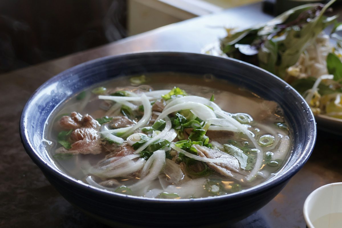 A bowl of beef pho with rice noodles, sliced onion and scallions