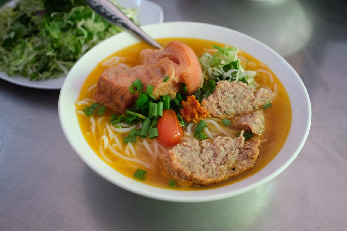 A bowl of bun bo Hue with rice noodles, pork, tomato and scallions